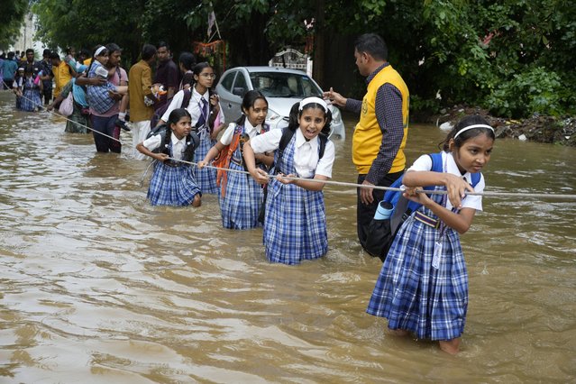 Students hold on to a rope as they cross a street flooded after heavy rains, on their way home in Ajmer, India, Friday, September 6, 2024. (Photo by Deepak Sharma/AP Photo)