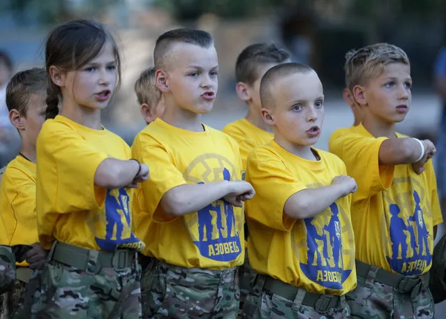 In this photo taken on Saturday, July 8, 2017, students at a paramilitary camp for children hit their fists onto their hearts during an evening ceremony outside Kiev, Ukraine. (Photo by Efrem Lukatsky/AP Photo)