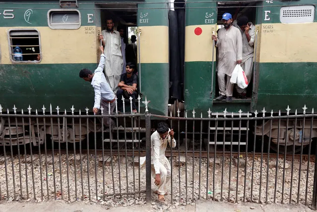 A man passes through a railing while others board a train as they make their way home, ahead of the Eid al-Fitr festival, at the Cantonment railway station in Karachi, Pakistan, July 5, 2016. (Photo by Akhtar Soomro/Reuters)