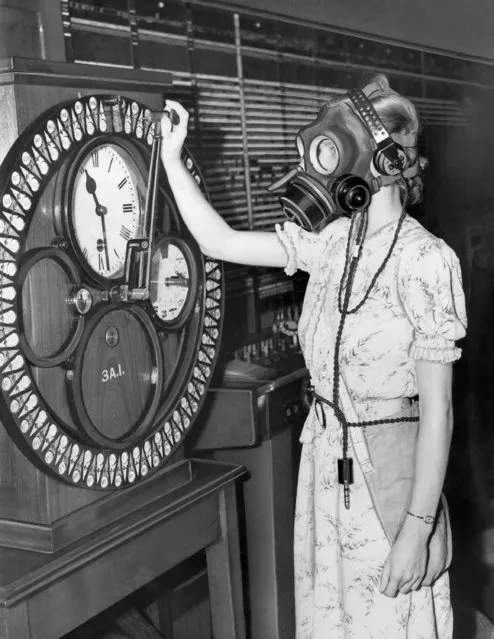 A London telephone operator demonstrates a special gas mask, equipped with built-in microphone and earpieces so that she could continue work even in the event of an air or gas raid. Here she punches a time clock. The demonstration took place at the Faraday Building trunk exchange, London, on August 3, 1938. (Photo by AP Photo)