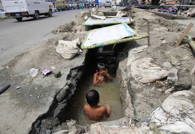 Children play in the murky waters of an open drainage being repaired by workers in Manila September 8, 2014. (Photo by Romeo Ranoco/Reuters)