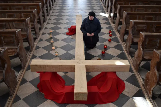 Catholic Christian believer kneels next to a giant cross during the Sunday service on April 5, 2020, in the town of Achmiany, some 130 km northwest of Minsk, during Palm Sunday celebrations which mark a week before Easter. (Photo by Sergei Gapon/AFP Photo)