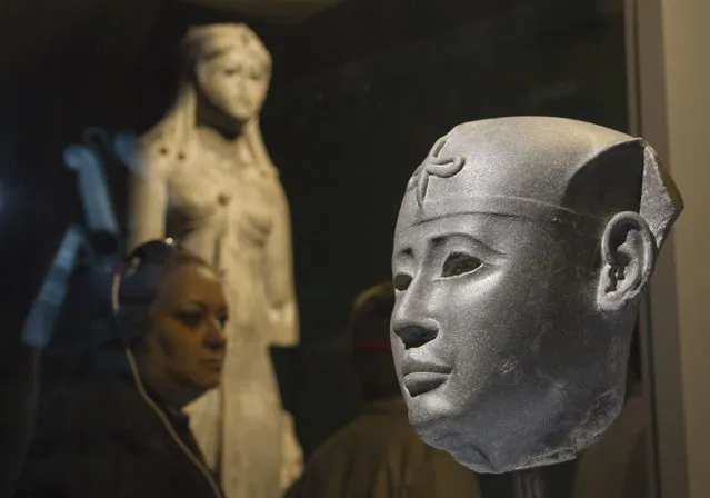 A woman looks on the head of a Pharaoh, 26th dynasty at the Institut du Monde Arabe (Arab World Institute), part of the Osiris, Sunken Mysteries of Egypt exhibition in Paris, France, Wednesday, September 9, 2015. As Paris-based UNESCO decries the destruction of ancient sites in Syria, Paris' Arab World Institute defiantly celebrates the preservation of ancient culture by holding a never-before-seen exhibit of the remains of the ancient Egyptian city of Heracleion, inaugerated by French President Francois Hollande. (Photo by Michel Euler/AP Photo)