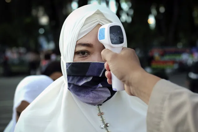 A security officer checks the temperature of a woman before she enters Baiturrahman Grand Mosque to attend an Eid al Fitr prayer in Banda Aceh in the deeply conservative Aceh province, Indonesia, Sunday, May 24, 2020. Millions of people in the world's largest Muslim nation are marking a muted and gloomy religious festival of Eid al-Fitr, the end of the fasting month of Ramadan – a usually joyous three-day celebration that has been significantly toned down as coronavirus cases soar. (Photo by Heri Juanda/AP Photo)
