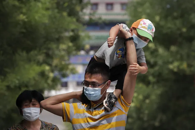 A man wearing a face mask to protect against the new coronavirus puts his masked child on his shoulders as they visit to a shopping district in Beijing, Sunday, July 19, 2020. China on Sunday reported another few dozen of confirmed cases of the coronavirus in the northwestern city of Urumqi, raising the total in the country's most recent local outbreak to at least 30. (Photo by Andy Wong/AP Photo)