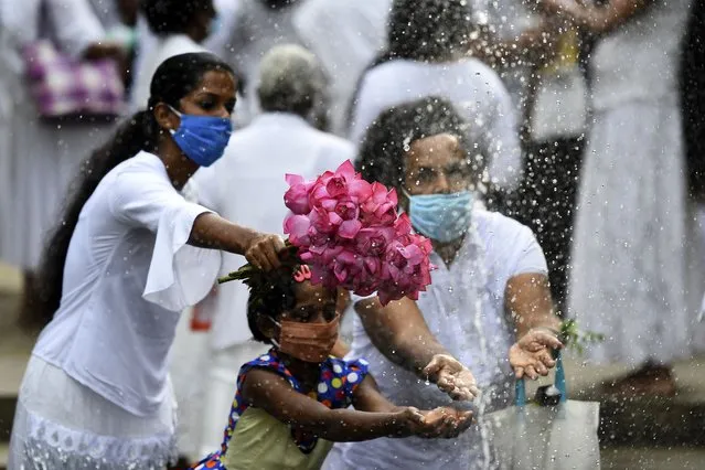 Buddhist devotees holds out flowers towards a fountain before praying during Poya, a full moon religious festival, at the Kelaniya Temple in the Kelaniya suburb of Colombo on July 4, 2020. (Photo by Ishara S. Kodikara/AFP Photo)