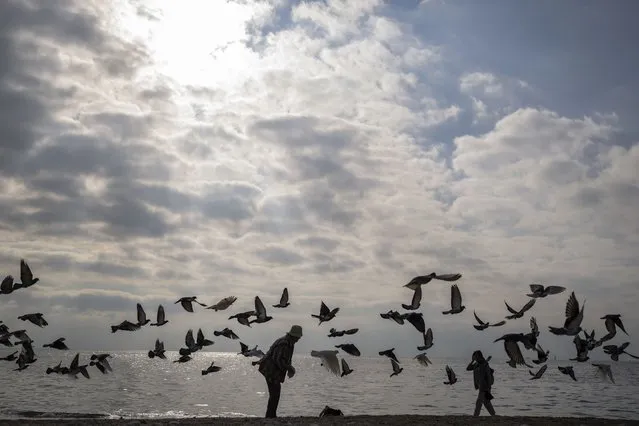 Pigeons fly as people walk on the beach in the Paleo Faliro suburb of southern Athens, Wednesday, December 28, 2022. (Photo by Petros Giannakouris/AP Photo)