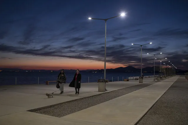 Two women with a dog wearing face masks to curb the coronavirus walk walk by the sea at Lipasmata Multifunctional Park in Drapetsona suburb of Piraeus, near Athens, on Monday, November 23, 2020 . A second nationwide lockdown was imposed earlier this month until the end of November but the restrictions are widely expected to be extended into December in some form. (Photo by Petros Giannakouris/AP Photo)