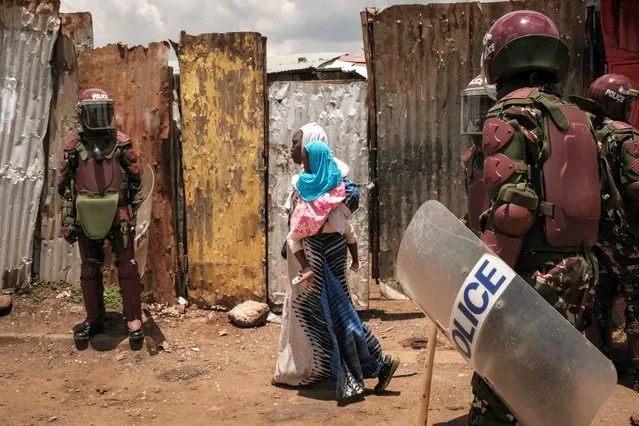 A woman holding a girl walks as police officers block the street during a rally called by the opposition leader Raila Odinga who claims the last Kenyan presidential election was stolen from him and blames the government for the hike of living costs in Kibera, Nairobi on March 27, 2023. Police fired tear gas to disperse anti-government protests on March 27, 2023 over the high cost of living, after the opposition vowed demonstrations would go ahead despite a police ban. (Photo by Yasuyoshi Chiba/AFP Photo)