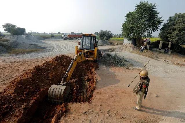 An excavator digs a ditch next to a national highway to stop the farmers, who are protesting against the newly passed farm bills, to cross a state border in Rewari district in the northern state of Haryana, near New Delhi, India, December 12, 2020. (Photo by Adnan Abidi/Reuters)