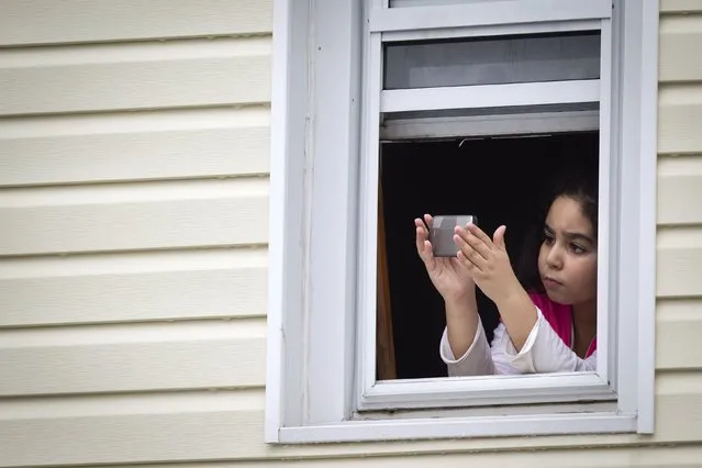 A child takes photos of slain New York Police Department officer Wenjian Liu's funeral from a window, in the Brooklyn borough of New York January 4, 2015. (Photo by Carlo Allegri/Reuters)