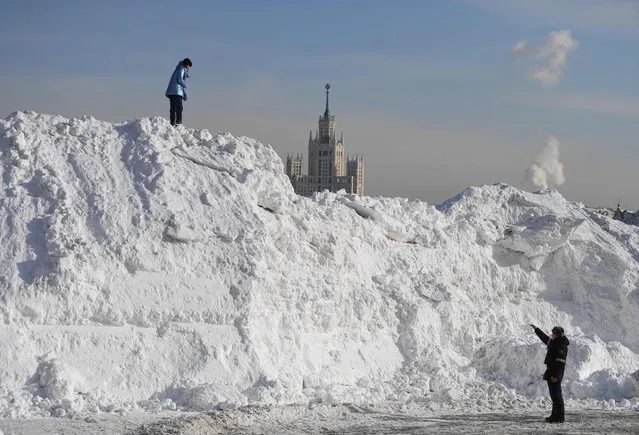 A Russian police officer talks to a woman as she walks on a huge pile of snow collected from the Red Square at Moscow's Vasilyevsky Spusk, during a frosty day and after heavy snowfalls on February 20, 2021. (Photo by Natalia Kolesnikova/AFP Photo)