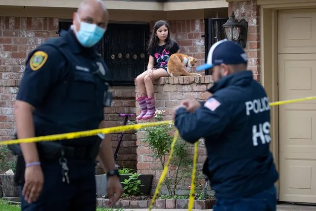 A young resident sits with a cat outside a home as police officials cordon off a street in southwest Houston, Texas, U.S., April 30, 2021. Dozens of persons were found inside a residence in Southwest Houston, which was initially reported as a kidnapping but prompted police to look into human smuggling, police and local news organizations reported. (Photo by Adrees Latif/Reuters)