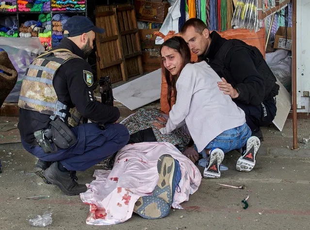 Policemen calm a woman by the body of her killed husband following a Russian rocket strike hitting a bus stop near a market in Kharkiv, Ukraine, 21 July 2022. At least three people were killed and 23 injured in the attack, according to the Kharkiv's Regional Prosecutor's Office. Kharkiv and surrounding areas have been the target of heavy shelling since February 2022, when Russian troops entered Ukraine starting a conflict that has provoked destruction and a humanitarian crisis. (Photo by Sergey Kozlov/EPA/EFE)