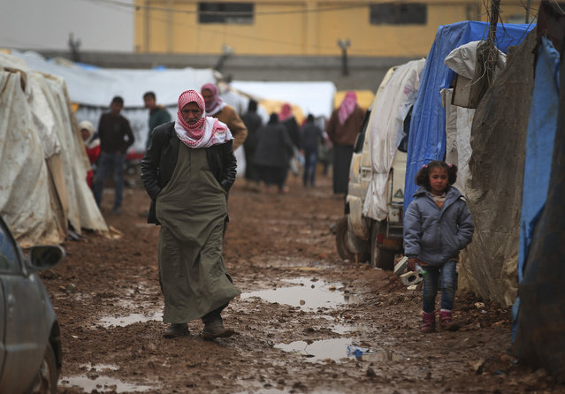 Syrian walk at a camp near the Bab al-Salam border crossing with Turkey, in Syria, Saturday, February 6, 2016. Thousands of Syrians have rushed toward the Turkish border, fleeing fierce Syrian government offensives and intense Russian airstrikes. Turkey has promised humanitarian help for the displaced civilians, including food and shelter, but it did not say whether it would let them cross into the country. (Photo by Bunyamin Aygun/AP Photo)