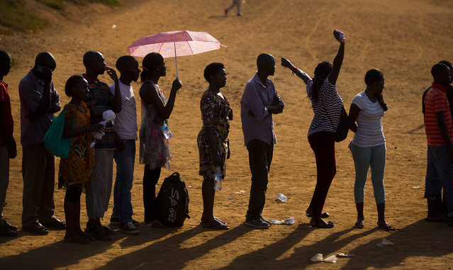 A voter stretches her arms as she and other Ugandans continue to queue to cast their votes at sunset in the capital Kampala, Uganda Thursday, February 18, 2016. Amid tardy delivery of voting materials, Ugandans tried to cast ballots Thursday in presidential and parliamentary elections, while a top international election observer called the delays “worrying” and the main opposition party said they were deliberate. (Photo by Ben Curtis/AP Photo)