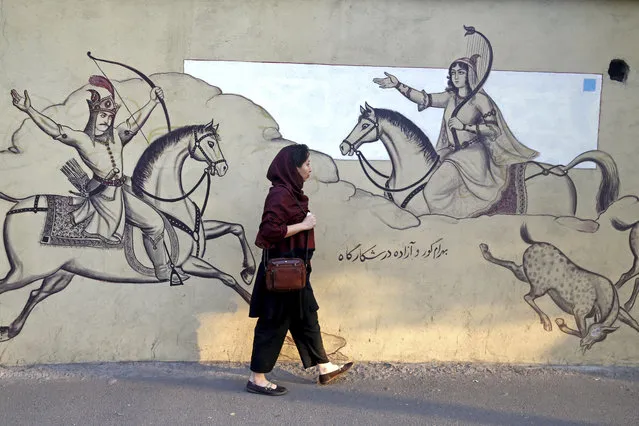 An Iranian woman walks past paintings of a Persian poetry in downtown Tehran, Iran, Monday, July 30, 2018. Iran's currency has dropped to a record low ahead of the imposition of renewed American sanctions, with many fearing prolonged economic suffering or possible civil unrest. (Photo by Ebrahim Noroozi/AP Photo)