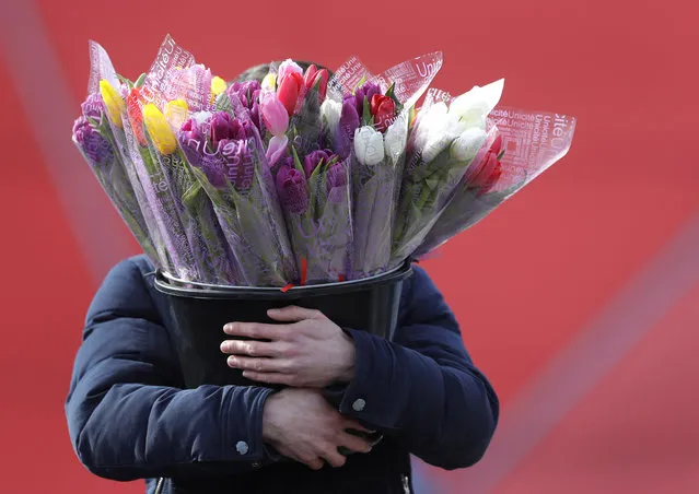 A man carries a bucket with bouquets of tulips at a street market on the eve of the International Women's Day in Minsk, Belarus, Thursday, March 7, 2019. International Women's Day on March 8 is an official holiday in Belarus, where men traditionally give flowers and gifts to female relatives, friends and colleagues. (Photo by Sergei Grits/AP Photo)