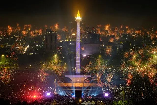 Fireworks explode over the city to usher in the New Year, as revellers gather around as the lit National Monument of Indonesia (MONAS) in Jakarta on January 1, 2024. (Photo by Yasuyoshi Chiba/AFP Photo)