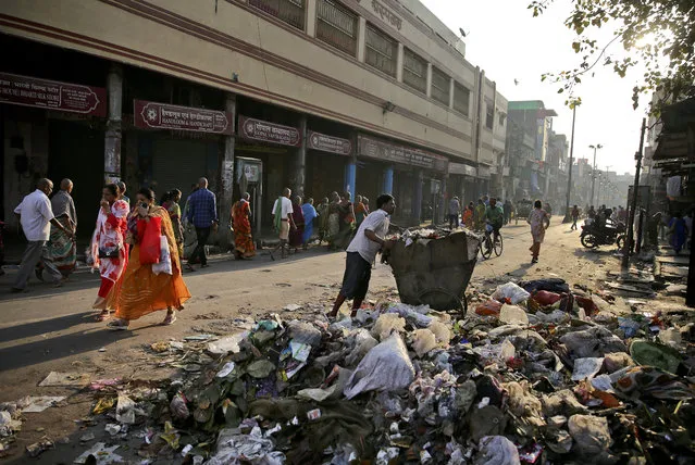 In this March 22, 2019 photo, people cover their noses as they walk past trash strewn on a street, in Varanasi, India. A project in the ancient Indian city of Varanasi dreamed up by Prime Minister Narendra Modi shows the master political marketer's penchant for symbolism as political strategy in elections that begin this month. (Photo by Altaf Qadri/AP Photo)