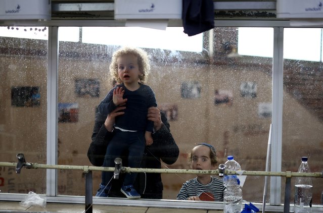 Orthodox Jewish children look through a window as they watch Orthodox Jewish men prepare matza, a traditional unleavened bread eaten during the upcoming Jewish holiday of Passover, at a bakery in Kfar Chabad, Israel, on April 18, 2024. (Photo by Hannah McKay/Reuters)