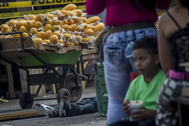 The body of a victim of a shootout between private security guards and gang members, lies next to a wheelbarrow filled with mangoes at the central market in San Salvador, El Salvador, Wednesday, March 15, 2017. At least 30 people, mostly gang members, died in the last 24 hours in El Salvador on one of the most violent days so far this year. (Photo by Salvador Melendez/AP Photo)