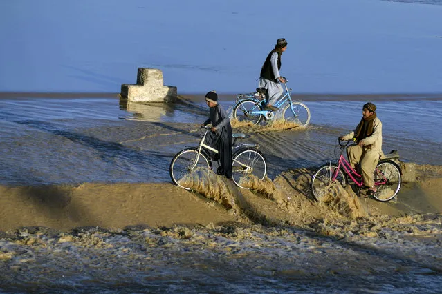 Boys ride bicycles on the flood waters flowing along a stream in Daman district of Kandahar on January 23, 2022. (Photo by Javed Tanveer/AFP Photo)