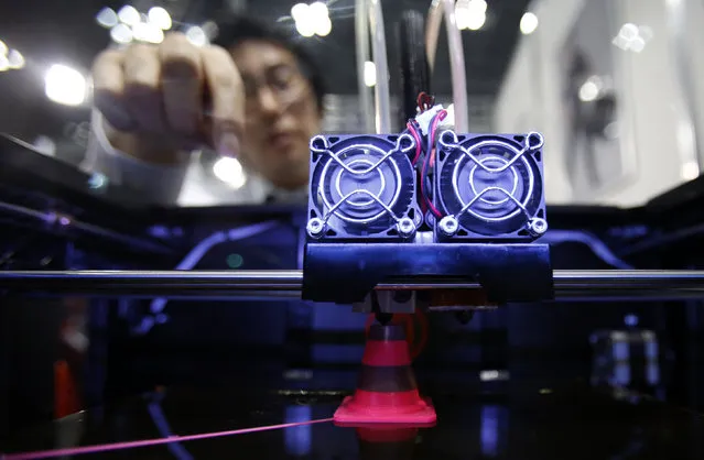 A staff member of Nihonbinary demonstrates their 3D printer MakerBot Replicator 2X as it prints an Acrylonitrile butadiene styrene pylon during the International Robot Exhibition 2013 in Tokyo November 8, 2013. (Photo by Yuya Shino/Reuters)