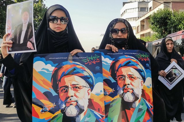 Mourners hold posters of Iranian President Ebrahim Raisi during a funeral ceremony for him and his companions who were killed in a helicopter crash, in Tehran, on May 22, 2024. Raisi was confirmed dead along with his foreign minister Hossein Amir-Abdollahian and six others on May 20, 2024, after search and rescue teams found their crashed helicopter in a fog-shrouded mountain region in Iran's East Azerbaijan province, sparking mourning in the Islamic republic. (Photo by Atta Kenare/AFP Photo)