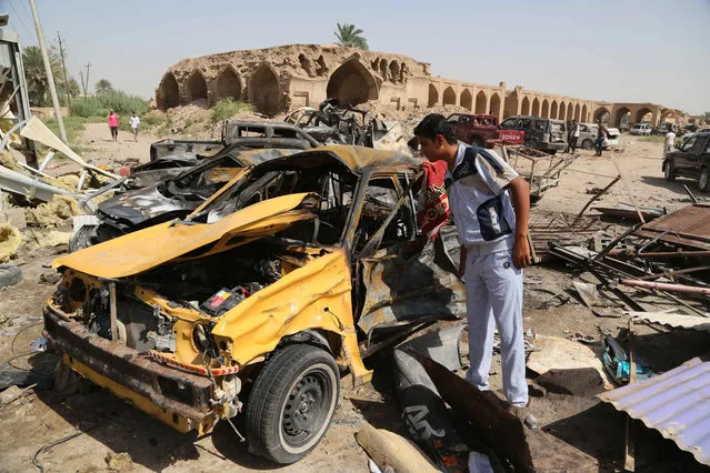 Civilians inspect the aftermath of a suicide car bombing at a busy market in Khan Bani Saad in the Diyala province, about 20 miles (30 kilometers) northeast of Baghdad, Iraq, Saturday, July 18, 2015. A suicide car bombing in Iraq's eastern Diyala province killed at least 80 people gathered at a marketplace to mark the end of the holy month of Ramadan on Friday. (Photo by Karim Kadim/AP Photo)