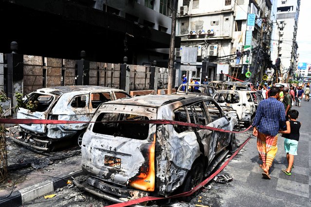 People walk past burnt vehicles after students set them on fire amid the ongoing anti-quota protest in Dhaka on July 19, 2024. (Photo by Munir Uz Zaman/AFP Photo)