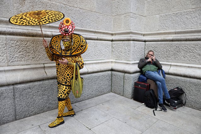 A person in costume is pictured next to a person waiting with bags during the annual Easter Parade and Bonnet Festival on 5th Ave in Manhattan, New York City, U.S., April 17, 2022. (Photo by Andrew Kelly/Reuters)