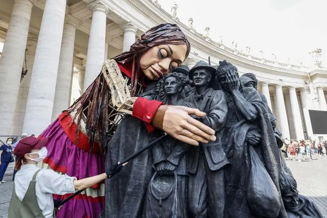 A 3.5 metre-tall puppet representing Amal, a young Syrian refugee, embraces the Angels Unawares, a bronze sculpture made by Timothy Schmalz representing a group of migrants, at its arrival in St. Peter's Square at the Vatican, September 10, 2021. The giant puppet, created by the Handspring Puppet Company, leads the 8,000 km itinerary festival named The Walk, started from Gaziantep, Turkey, and expected to arrive in Manchester, UK, after traveling across Greece, Italy, France, Switzerland, Germany and Belgium to focus public attention on young refugees. (Photo by Riccardo De Luca/Anadolu Agency via Getty Images)