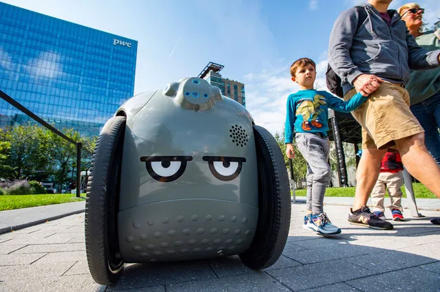 People walk by Gita, a robot by Piaggio, as it travels around the park at the Robot Block Party put on by MassRobotoics in Boston, Massachusetts on October 2, 2021. Leading Robotic companies showcased their latest products as well as design concepts to introduce the public to the future in robotics, from drones to autonomous cars. (Photo by Joseph Prezioso/AFP Photo)