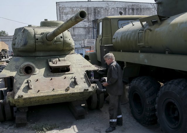 A worker looks at an old soviet tank T-34 (L) as he fixes military vehicle (R) at a Phaeton museum in Zaporizhia, Ukraine, August 11, 2015. (Photo by Gleb Garanich/Reuters)