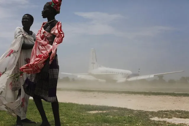 Women try to avoid dust as a plane, carrying nutrition supplements brought in by Medecins Sans Frontieres (MSF), lands in Leer July 15, 2014. The MSF hospital was giving service to over 200,000 people before it was looted and burned during fighting in late January and early February. The Hospital currently attends 1400 malnourished children according to Medecins Sans Frontieres. (Photo by Andreea Campeanu/Reuters)