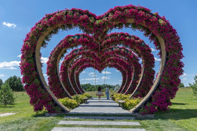 A woman swings from a heart-shaped flower installation in Dobro Park, Motyzhyn, Kyiv region, Ukraine, Wednesday, June 26, 2024. Despite hardships brought by war flowers fill Kyiv and other Ukrainian cities. They burst out of planters that line the capital's backroads and grand boulevards and are fixed to lampposts. (Photo by Anton Shtuka/AP Photo)
