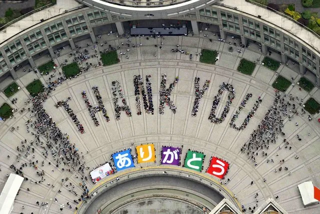 An aerial view shows people sitting in formation to the words “thank you” and displaying signs that collectively read “Arigato” (Thank You) during an event celebrating Tokyo being chosen to host the 2020 Olympic Games, at Tokyo Metropolitan Government Building in Tokyo, in this file photo taken by Kyodo September 8, 2013. Tokyo's 2020 Summer Olympics were meant to be different: compact, on budget and on time. (Photo by AFP Photo/Kyodo)