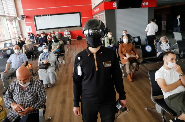 A security employee wearing a thermal imaging VF helmet monitors passengers as they wait for to board an Anadolujet flight to Stuttgart, Germany at Sabiha Gokcen Airport during the first day of resumed international flights that were halted amid the spread of the coronavirus disease (COVID-19), in Istanbul, Turkey on June 11, 2020. (Photo by Murad Sezer/Reuters)