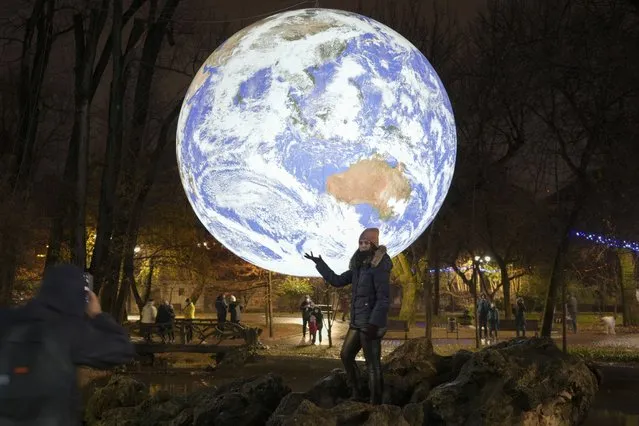 A girl poses by a depiction of Earth, a light installation by British artist Luke Jerram in Bucharest, Romania, Saturday, December 11, 2021. Romania relaxed some of its COVID-19 pandemic restrictions, among which face masks are no longer mandatory outdoors in uncrowded areas, as Health minister Alexandru Rafila said that the authorities must give people hope that they can “live normally in this country” but that if infection rates rise above certain thresholds, measures will be reversed. (Photo by Vadim Ghirda/AP Photo)