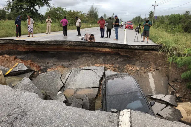 People take photos of a road that collapsed due to heavy flooding in the southern Thai district of Songkhla on November 30, 2017. Heavy floods swept into southern Thailand this week killing five people, authorities said on November 30 as photos of waterlogged and damaged roads spread on social media. (Photo by Tuwaedaniya Meringing/AFP Photo)