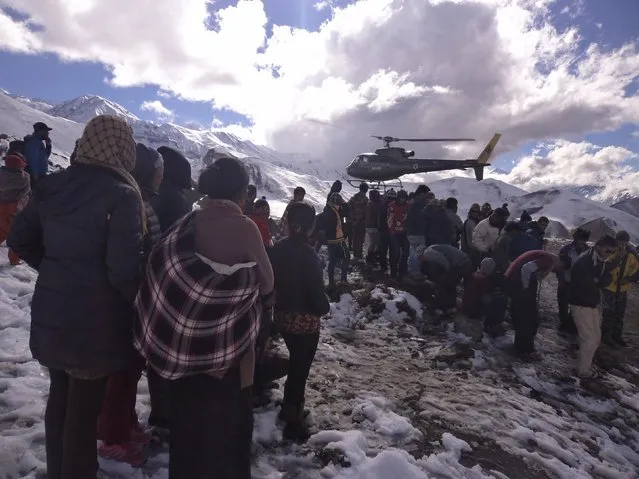 People gather near a helicopter belonging to Nepal Army used to rescue avalanche victims at Thorang-La in Annapurna Region in this October 15, 2014 handout photo provided by Nepal Army. At least 12 people, including eight foreign hikers and a group of yak herders, were killed in Nepal by unseasonal blizzards and avalanches triggered by the tail of cyclone Hudhud, officials said on Wednesday. (Photo by Reuters/Nepalese Army)
