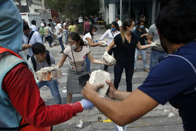 Volunteers pick up the rubble from a building that collapsed during an earthquake in the Condesa neighborhood of Mexico City on September 19, 2017. Survivors quickly rallied, clambering over grotesque ruins of buildings and joining professional rescue workers to try to save friends, neighbors and strangers. (Photo by Rebecca Blackwell/AP Photo)