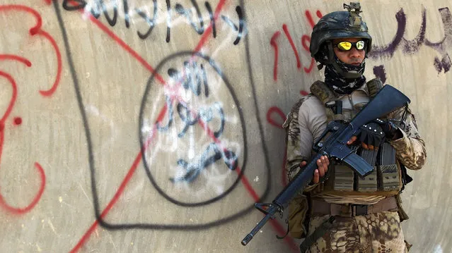 An Iraqi soldier stands next to a wall with a red cross above a slogan of the Islamic State (IS) group, on September 4, 2016 in the city of Fallujah. Iraq's security forces have for months been battling IS fighters in Anbar province, notching up key victories in provincial Ramadi and jihadist bastion Fallujah earlier this year. (Photo by Ahmad Al-Rubaye/AFP Photo)