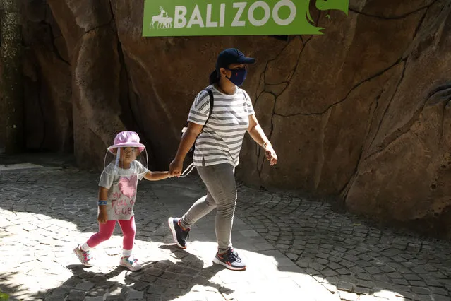 A mother walks with her daughter wearing protective gear during their visit to the zoo in Bali, Indonesia, Monday, July 13, 2020. Indonesia's resort island of Bali reopened after a three-month virus lockdown last week, allowing local people and stranded foreign tourists to resume public activities before foreign arrivals resume in September. (Photo by Firdia Lisnawati/AP Photo)