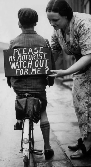 A mother fastening a notice reading “Please Mr Motorist, watch out for me”, onto her son's back before he sets out on a trial bicycle ride in UK, 40s. (Photo by Hulton Collection/Getty Images)