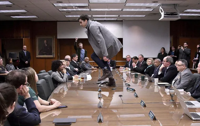 Michigan State student Connor Berry, 22, climbs atop the table to make a statement in protest to the vote, as the MSU board of trustees meets and votes to name former Gov. John Engler as their interim president, in East Lansing, Mich., Wednesday, January 31, 2018. Engler was formally named interim president at Michigan State, following Lou Anna Simon's resignation last week from the school's top post. (Photo by Dale G.Young/Detroit News via AP Photo)