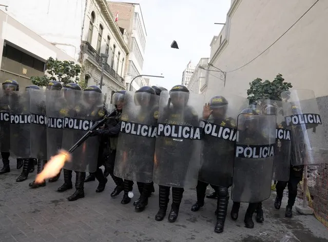 A police officer in riot gear fires his shotgun to disperse anti-government protesters who traveled to the capital from across the country to march against Peruvian President Dina Boluarte, as they clash in Lima, Peru, Thursday, January 19, 2023. Protesters are seeking immediate elections, Boluarte's resignation, the release of ousted President Pedro Castillo and justice for up to 48 protesters killed in clashes with police. (Photo by Martin Mejia/AP Photo)