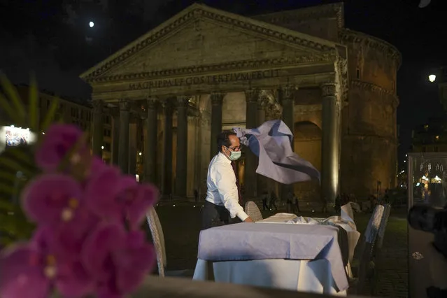 A waiter clears a table before closing a restaurant in front of the Pantheon, Rome, Monday, October 26, 2020. For at least the next month, people outdoors except for small children must now wear masks in all of Italy, gyms, cinemas and movie theaters will be closed, ski slopes are off-limits to all but competitive skiers and cafes and restaurants must shut down in early evenings, under a decree signed on Sunday by Italian Premier Giuseppe Conte, who ruled against another severe lockdown despite a current surge in COVID-19 infections. (Photo by Andrew Medichini/AP Photo)