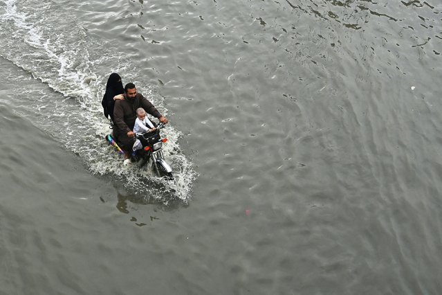 Commuters wade through a flooded street after heavy rainfall in Karachi on September 10, 2025. (Photo by Asif Hassan/AFP Photo)